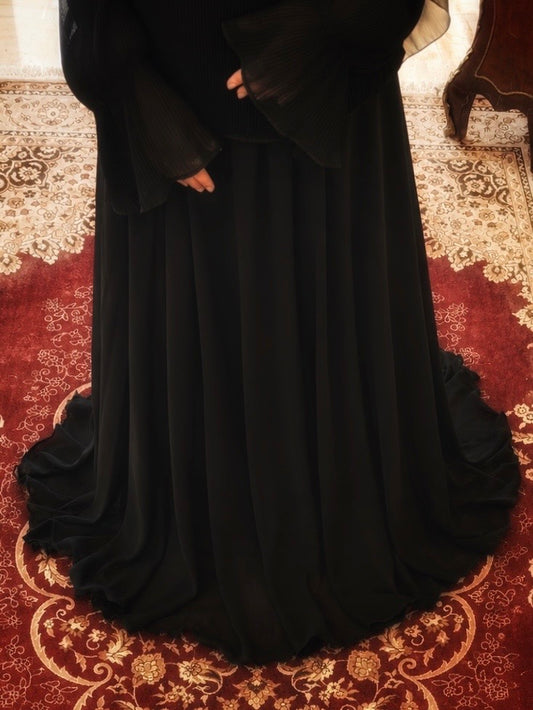 A long flowing black dress or abaya with wide sleeves, shown on a person standing on a red and gold patterned rug indoors.