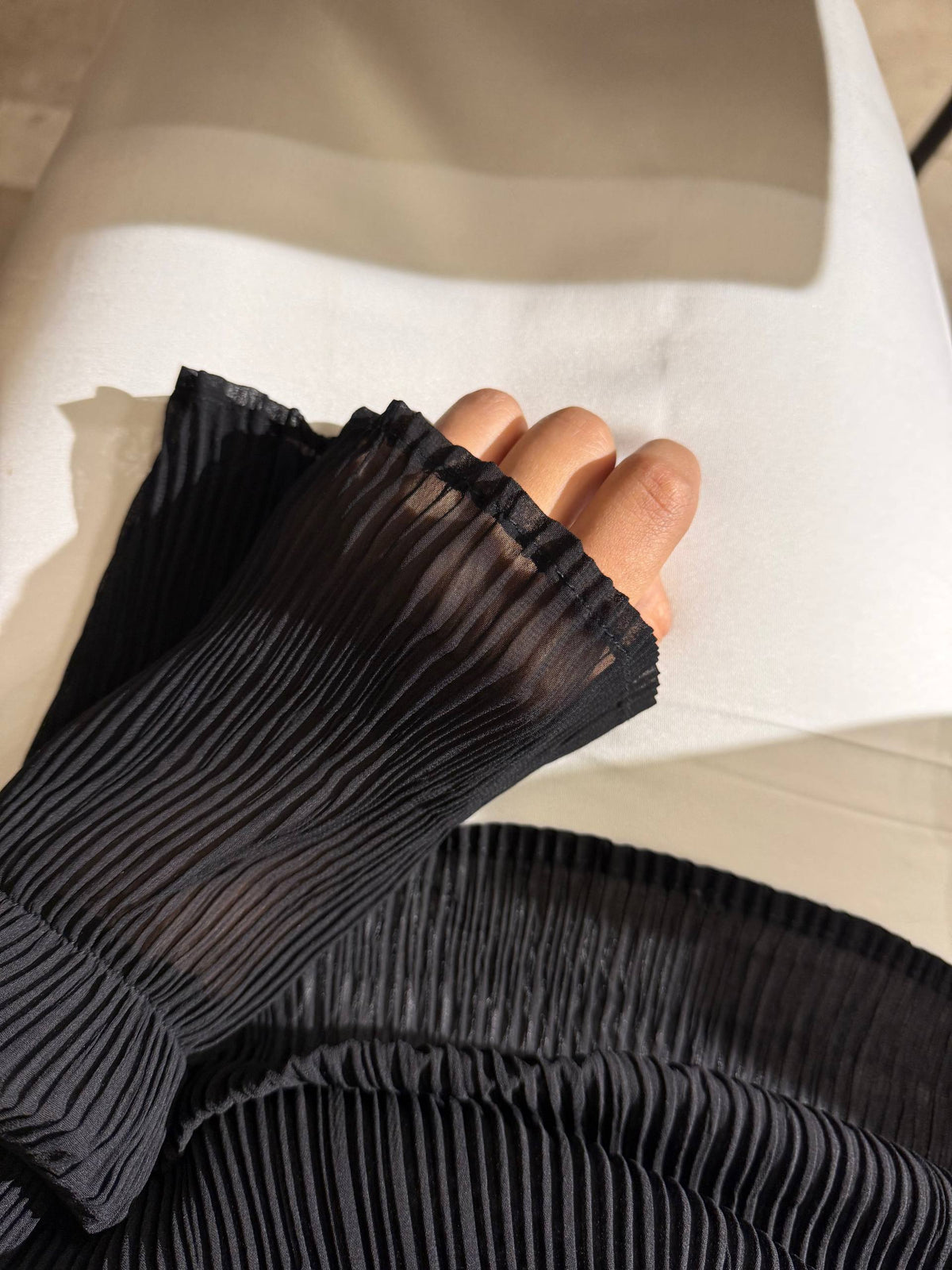 A close-up of a person's hand wearing a black pleated, semi-sheer long sleeve or glove, resting on a white surface.