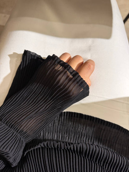 A close-up of a person's hand wearing a black pleated, semi-sheer long sleeve or glove, resting on a white surface.